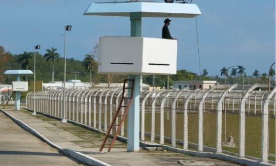Vista de una prisión en Cuba con torres de vigilancia, un guardia en lo alto y cercas perimetrales con alambre de púas.
