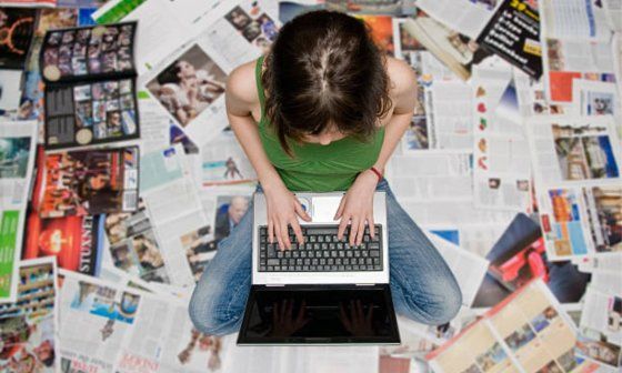 Muchacha escribe en laptop en medio de muchos periódicos dispersos por el suelo