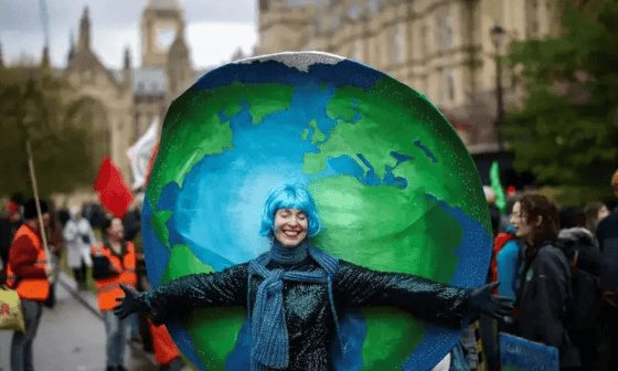 Persona sosteniendo una pelota pintada como el planeta Tierra durante la protesta The Big One en Londres.