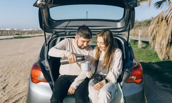 Pareja se sirve una bebida mientras descansa junto a su coche durante un viaje por Italia