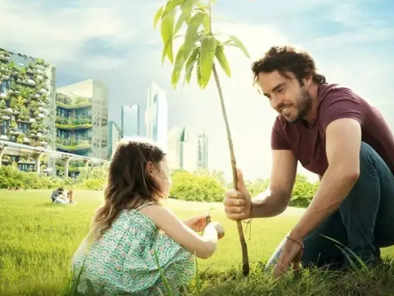 Fotograma del documental "2040" muestra a un hombre y una niña sembrando una planta en un capo verde con la ciudad al fondo.